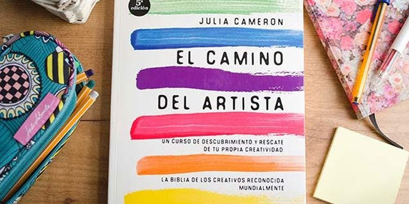 La foto muestra el libro de Julia  Cameron, junto a un  estuche de  lápices, un cuaderno  floral con bolígrafos, además de un paquete de pósits amarillos 